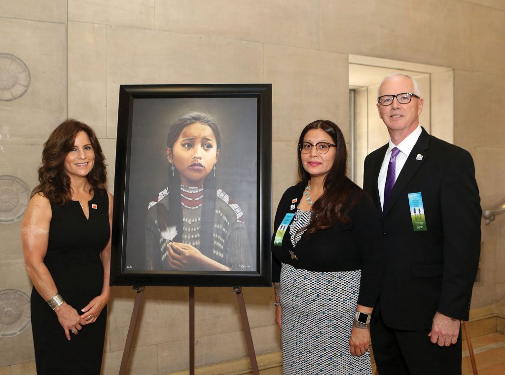 Three people with the painting "Never Forgotten"