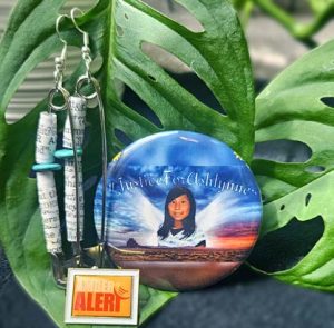 Sibling-survivor Kimber Biggs photographed her AMBER Alert lapel pin and two gifts from Ashlynne’s mother, Pamela Foster: a memorial button and a pair of earrings with wording from the Ashlynne Mike AMBER Alert in Indian Country Act of 2018.
