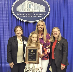 AATTAP Administrator Janell Rasmussen congratulates the 2024 National Missing Children’s Day poster winner, Hanna L., a fifth grader from Chesnee, South Carolina. She and Hanna are shown with Hanna’s mother (back) and South Carolina AMBER Alert Coordinator Alex Schelble (right).