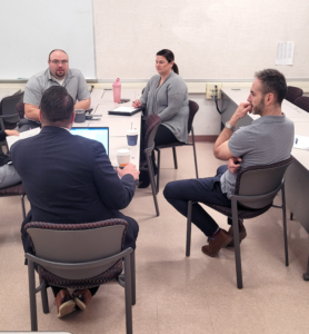 Photo of three men and a woman sitting around a table talking with AATTAP in Canada.