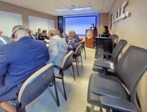 Photo of people sitting at a table listening to a AATTAP Administrator Janell Rasmussen, standing behind a podium in Puerto Rico.