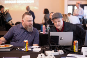 Two men looking at a computer monitor screen in a crowded room.