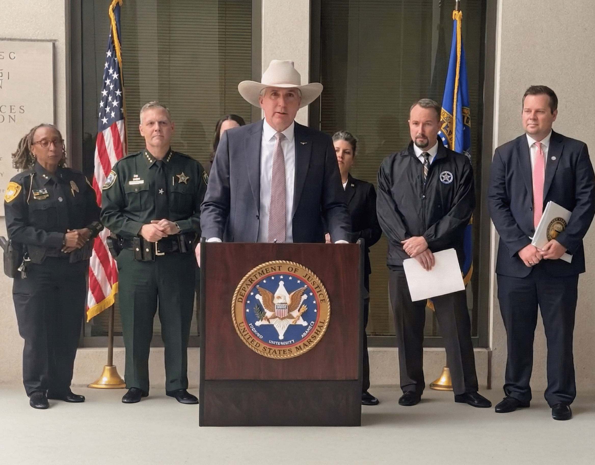 Man in cowboy hat at podium flanked by colleagues at a press conference for the U.S. Marshals