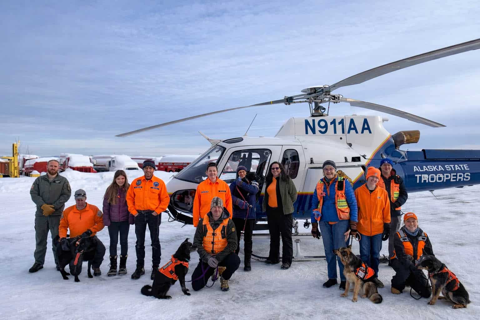 Group of Alaska State Troopers and volunteers in front of a helicopter on a snow-packed environment