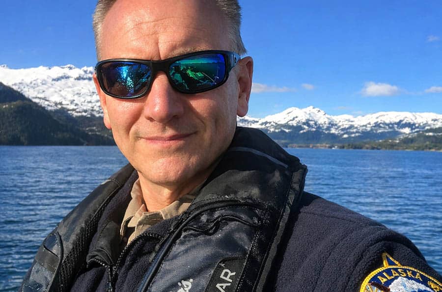 Photo of man wearing sunglasses with watery, mountainous Alaska in the background