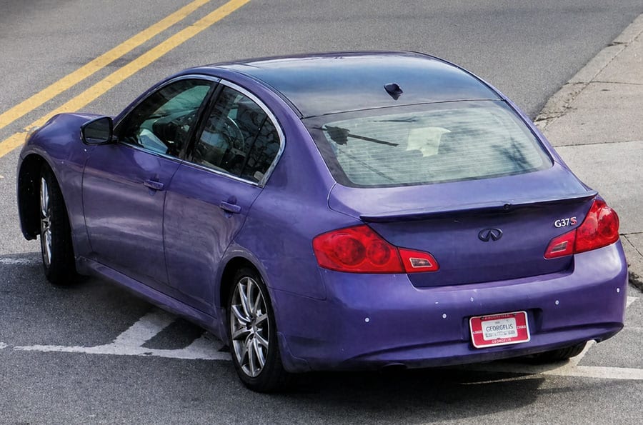 Purple Infiniti G37S with temporary plates turning a corner.