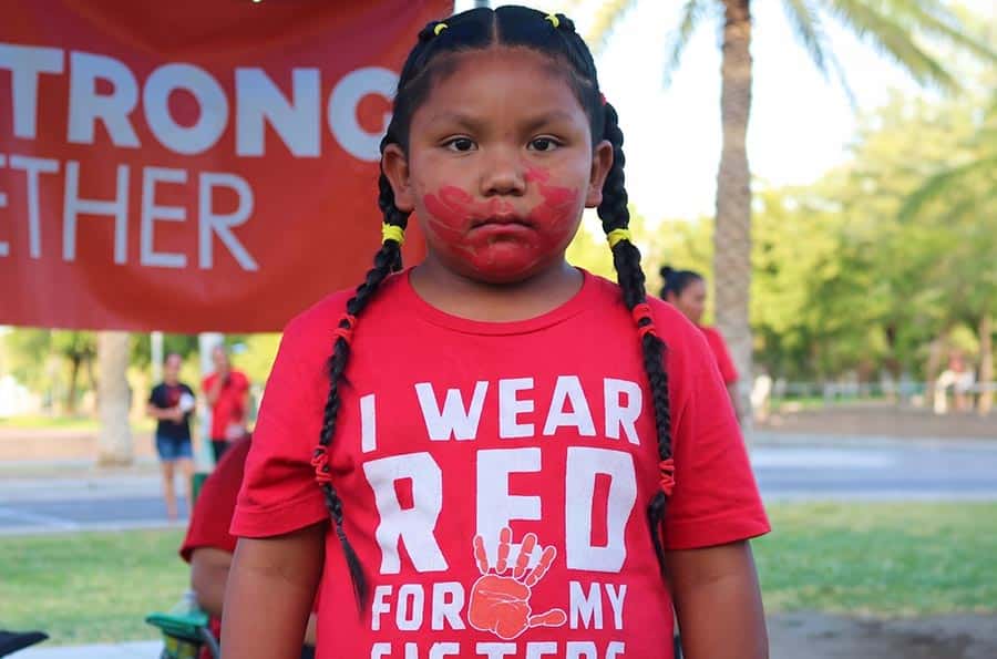 A young girl wearing a red shirt with the words "I wear red for my sister" on it, and with a red face paint hand print on face.