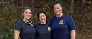 Lisa Vorrasi with two female coworkers wearing police tshirts and standing at edge of woods