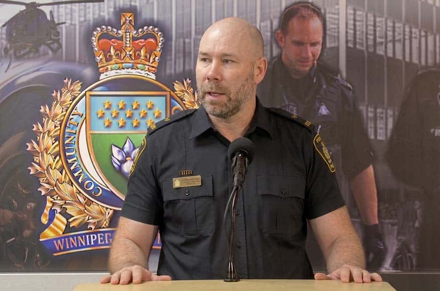 Winnipeg Manitoba Police Chief briefing media at podium in front of wall graphic with the agency crest and collage of officers