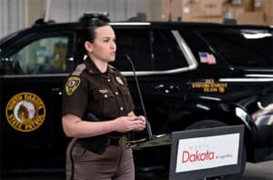 Lieutenant Jenna Clawson Huibregtse speaking at a podium with a North Dakota State Patrol SUV in the background