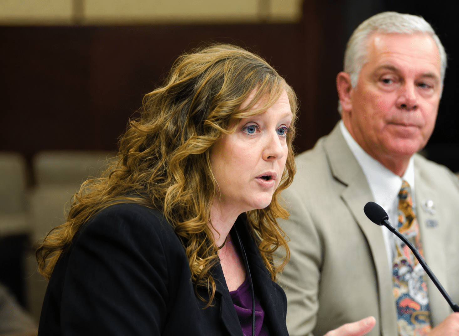 Photo of a woman (Janell Rasmussen) speaking at a table with microphone