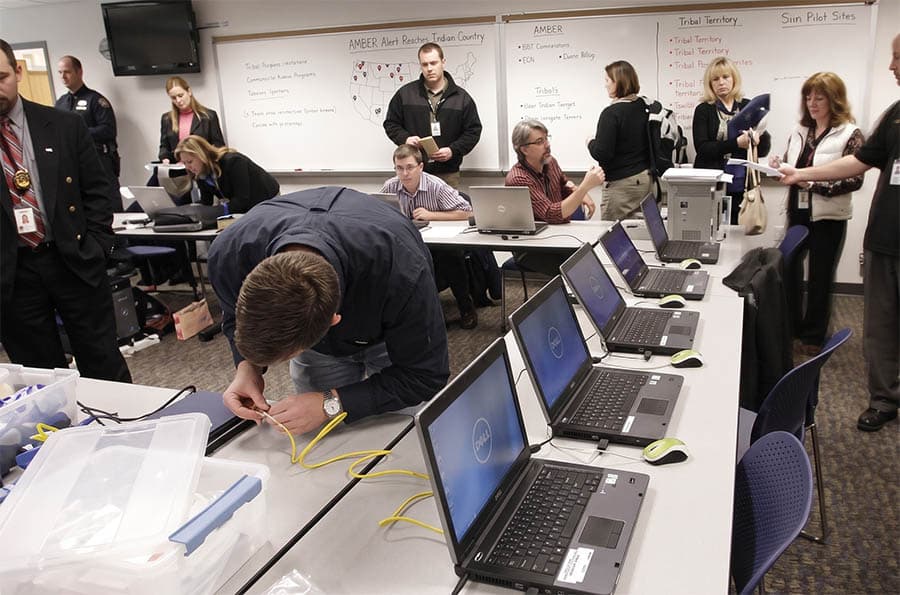 Child Abduction Response Team in an operations room with laptops and whiteboards filled with info.