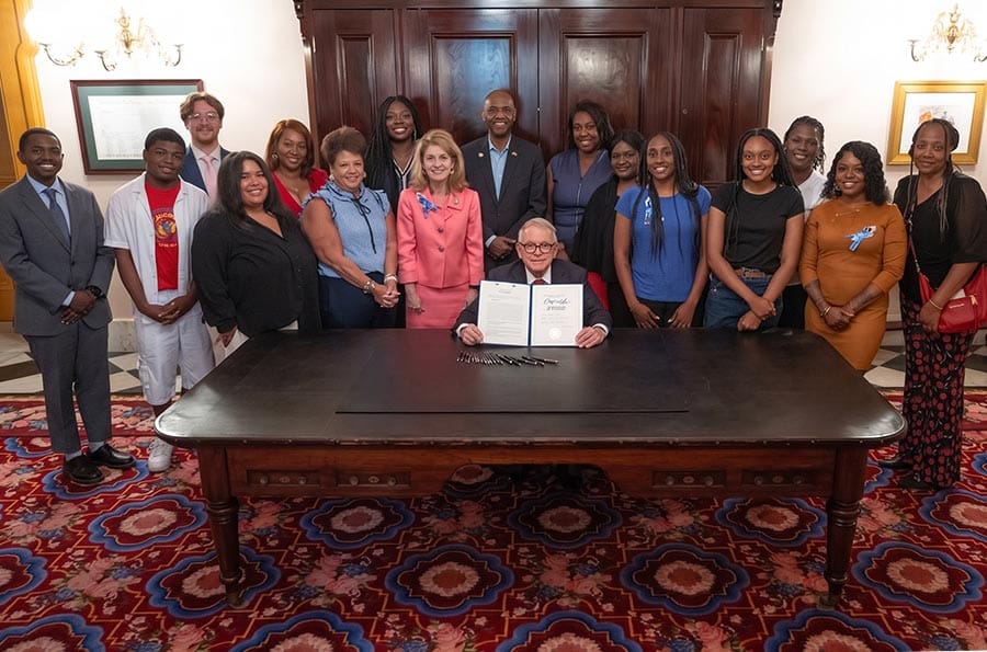 Ohio Gov. DeWine holding up Joshua Alert Act at signing ceremony surrounded by Joshua's family.
