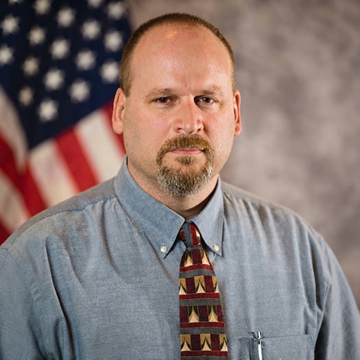Photo of Derek Welsh in front of a U.S. flag
