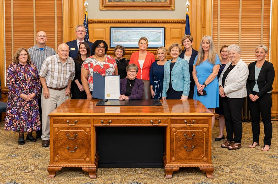 Missouri Governor bill signing ceremony for RJ Law Purple Alert. Group pose at large desk. Seated woman holding the signed document.