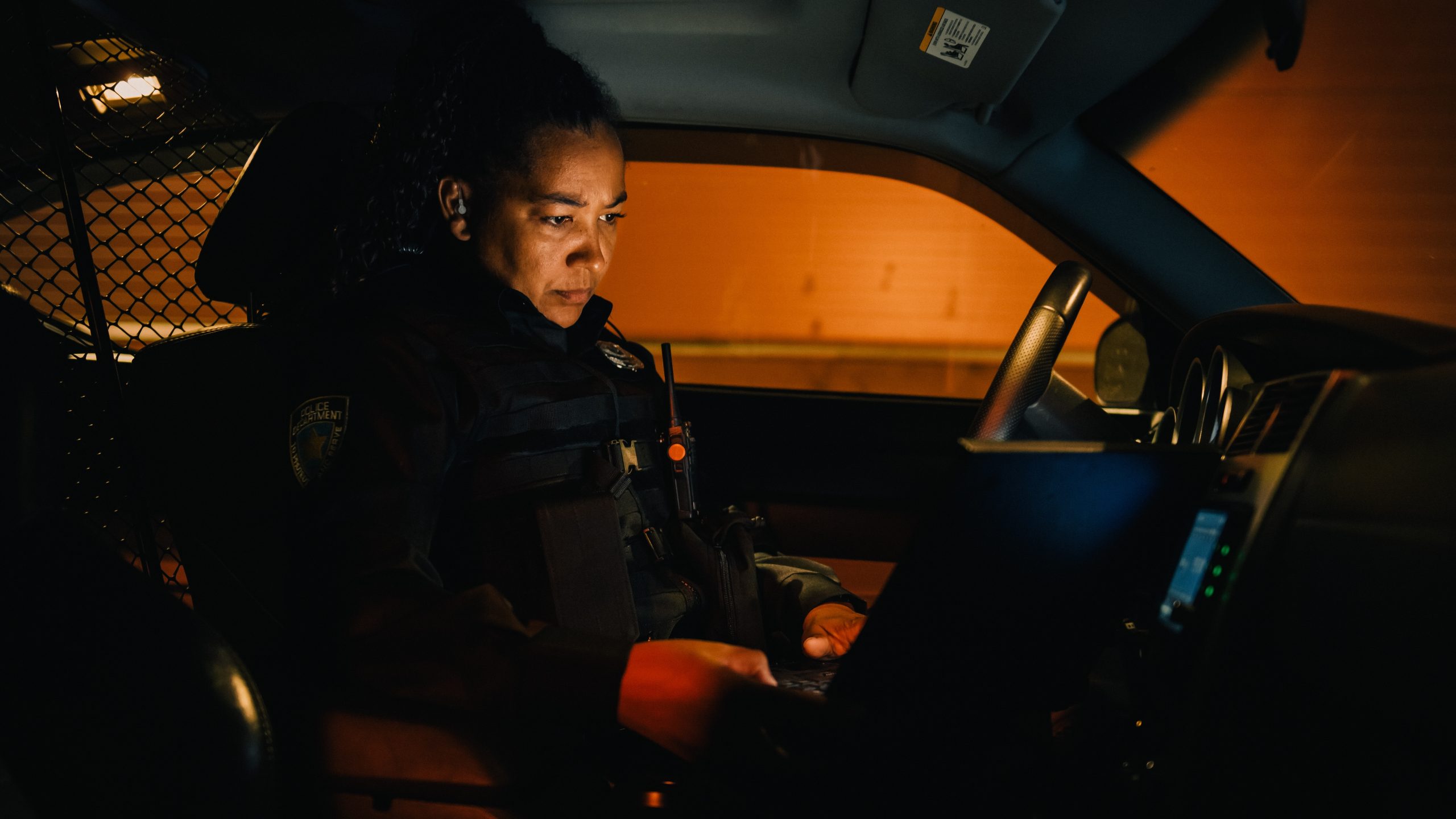 Female police officer in patrol vehicle at night, looking at mobile computer